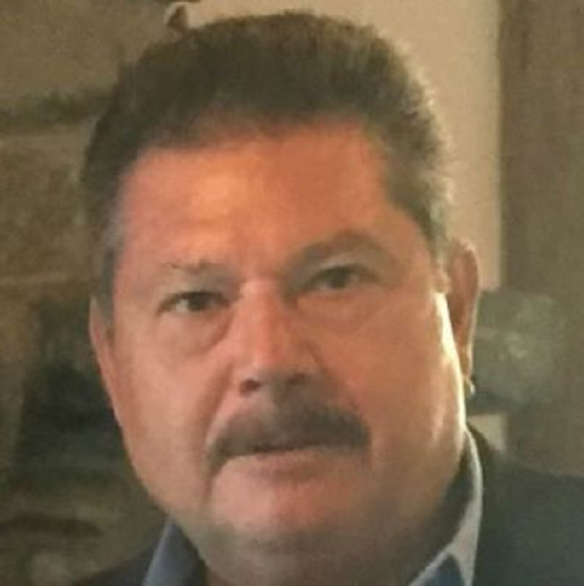 Mustachioed man faces camera, unsmiling